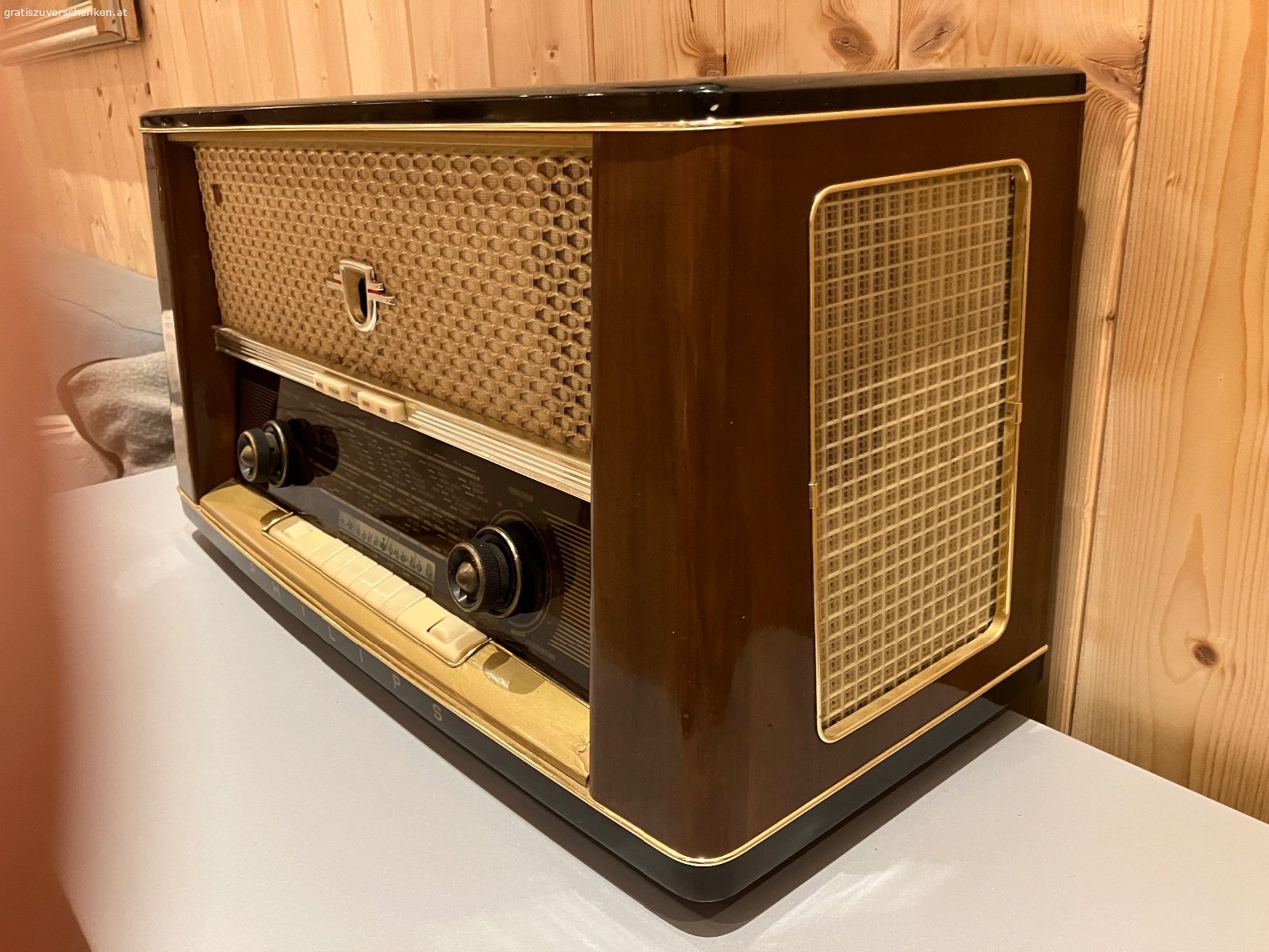 Alter Philips Röhrenradio / Vintage-Radio – funktionstüchtig. Verschenke einen alten Philips Radio im klassischen Holzgehäuse aus früheren Jahrzehnten.

Das Gerät ist funktionstüchtig und auch optisch für sein Alter noch in einem schönen Zustand. Ein dekoratives Stück für Liebhaber alter Radios, Sammler oder auch als Vintage-Dekoration.

Der Radio verfügt über die klassischen Wellenbereiche LW, KW, MW und UKW sowie verschiedene Klangtasten.

Der Lautstärkeregler sollte einmal gereinigt bzw. gewartet werden, ansonsten funktioniert das Gerät. Aufgrund des Alters wird es natürlich ohne Garantie auf dauerhafte Funktion abgegeben.

Abmessungen ca.:

* Breite: 60 cm
* Höhe: 38 cm
* Tiefe: 24 cm

Das schöne Holzgehäuse, die große Senderskala und die typische Stoffbespannung machen den Philips auch optisch zu einem schönen Zeitzeugen.

Gratis gegen Selbstabholung.
Vielleicht findet sich ein Liebhaber, der Freude daran hat und den Radio weiter verwendet oder restauriert.

Privatabgabe, keine Garantie oder Gewährleistung.